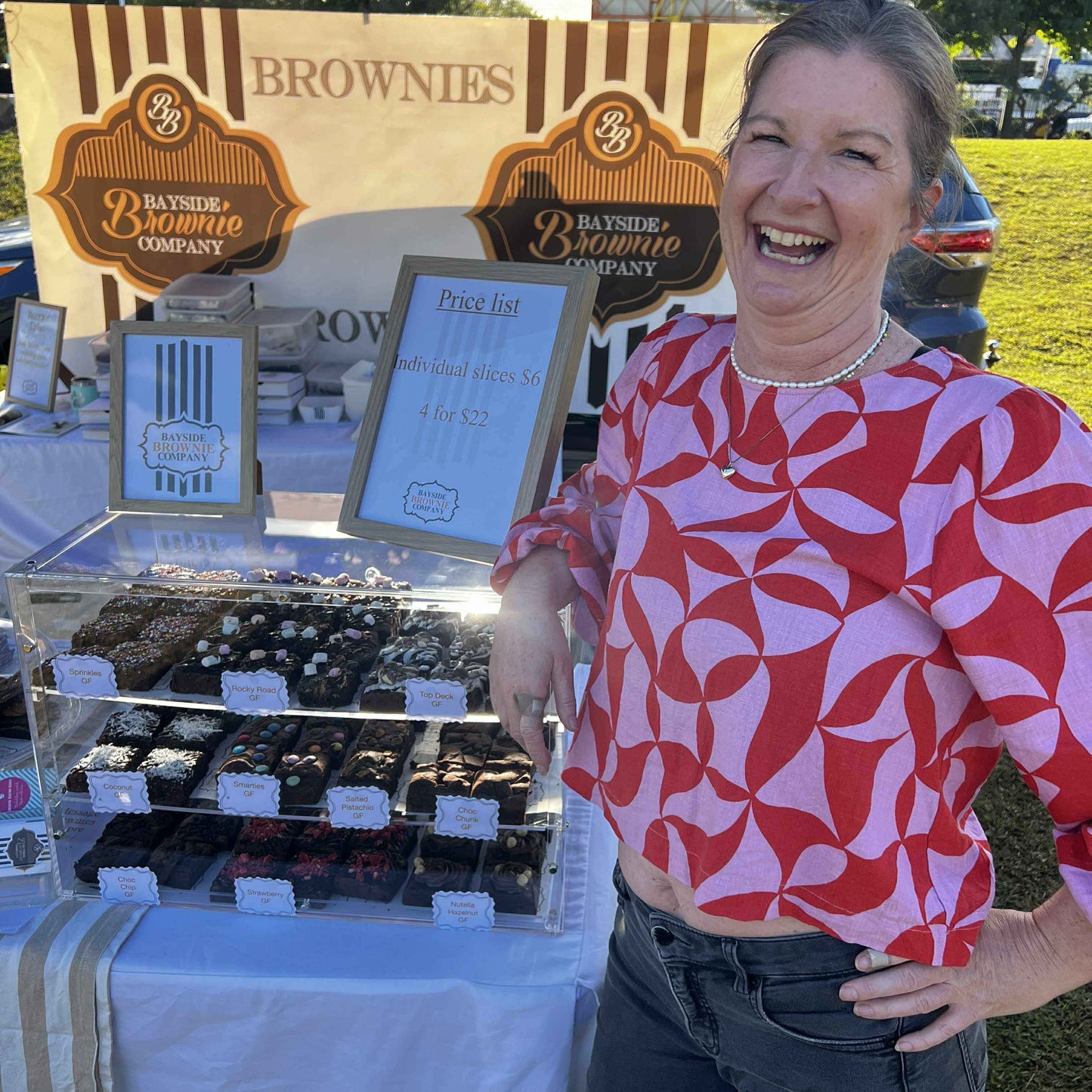 Woman standing next to a display of brownies at a booth with 'Bayside Brownie Company' branding.